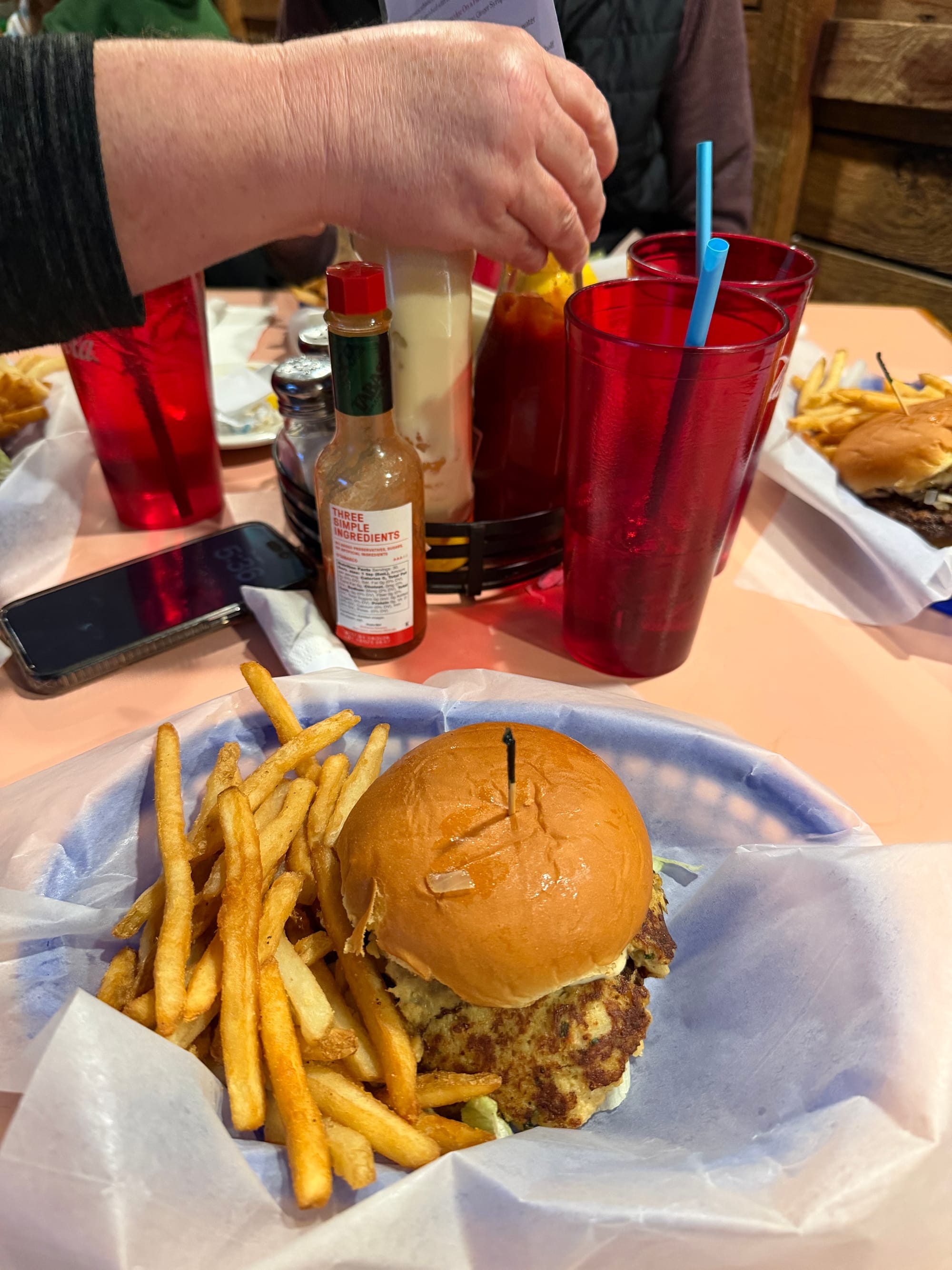 A crab smash burger in a plate with fries on the side and sweet tea in the back.