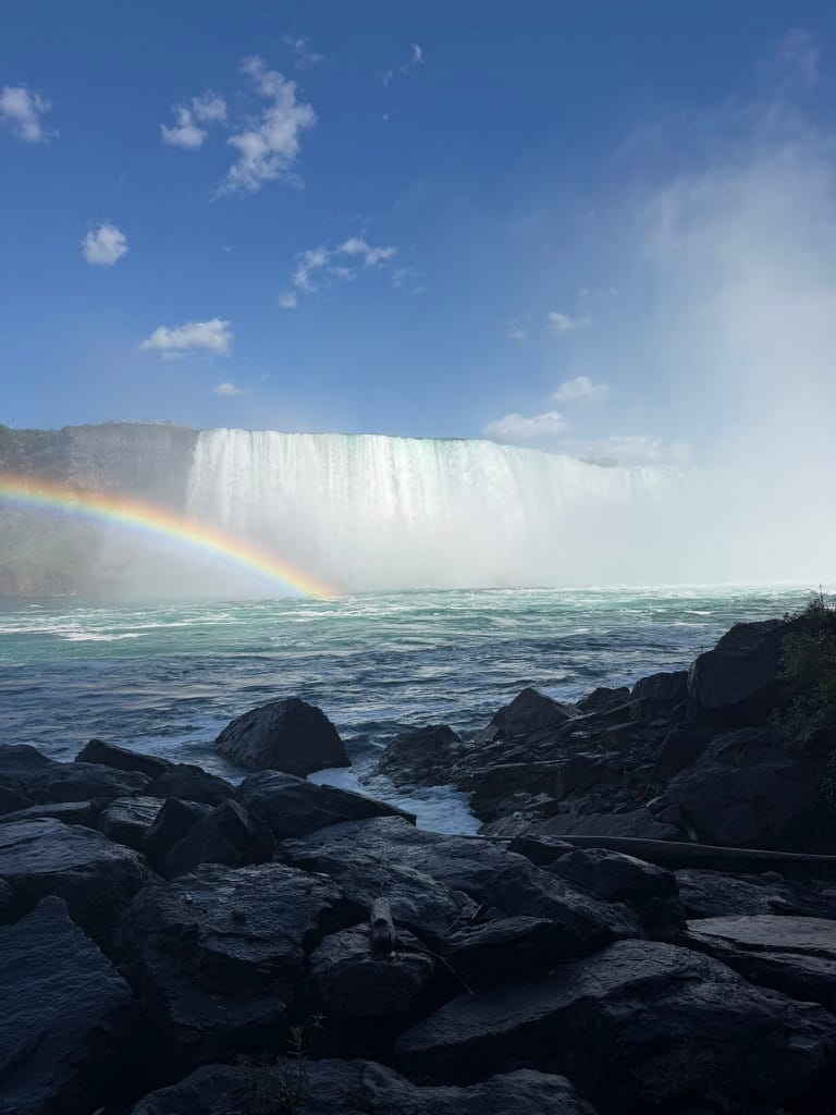 The falls are in the background with mist and a rainbow in the middle. There are rocks in the foreground.
