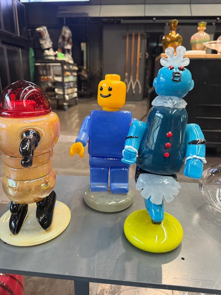 Some figures made from glass with a Lego minifigure made of glass in the middle.