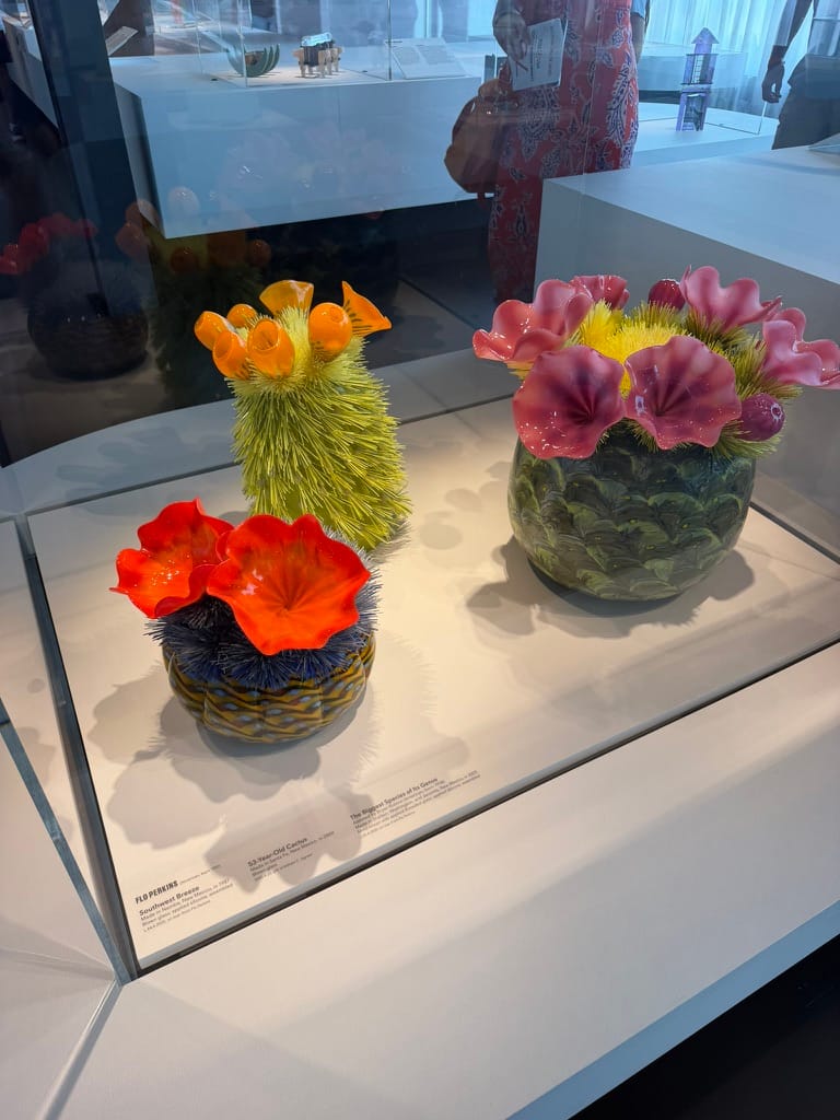 Three cacti made of glass shards and blown glass in a display case.