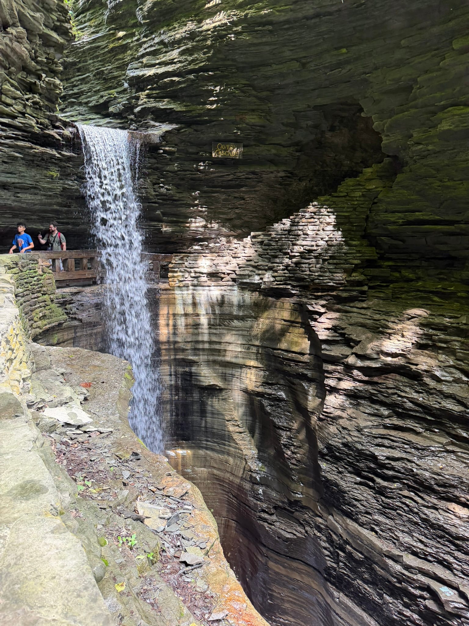 A path goes behind a waterfall flowing down from above and the bottom out of frame.