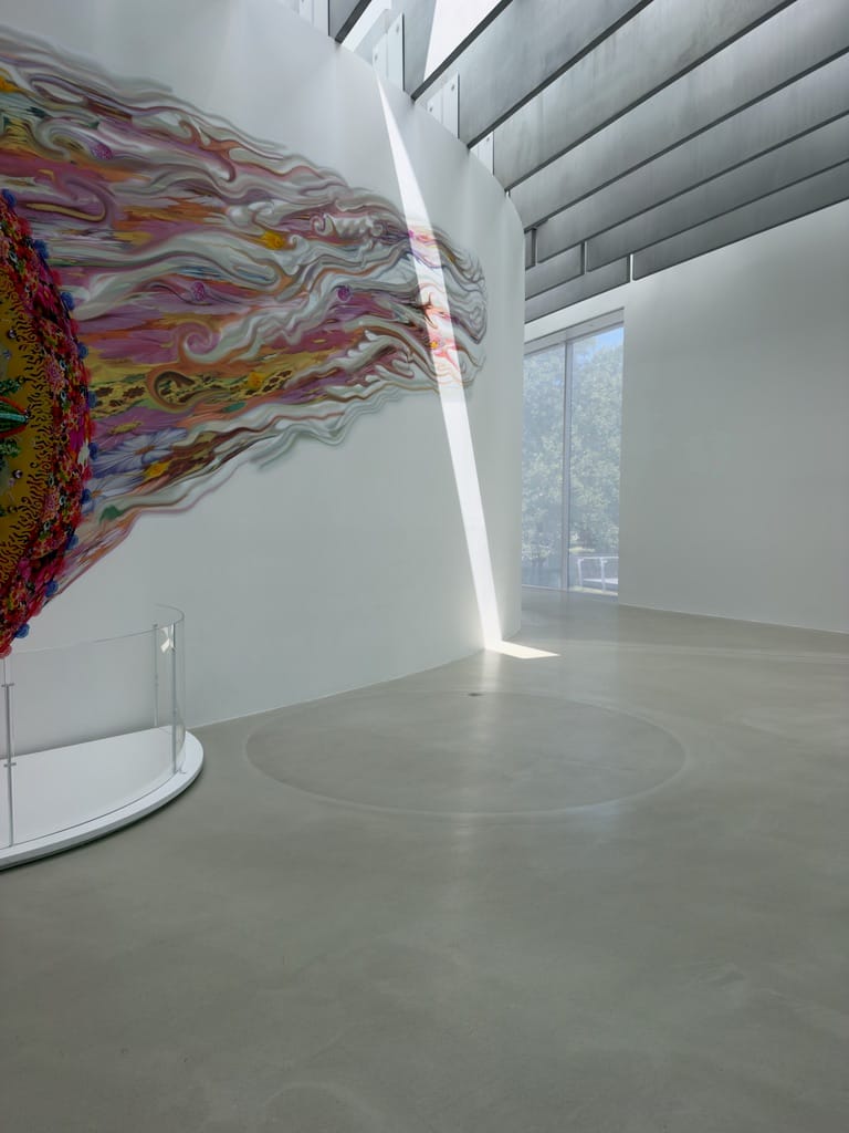 A large colorful art piece is partially visible on the left. It has a tail that leads into a ray of light cutting through the space.