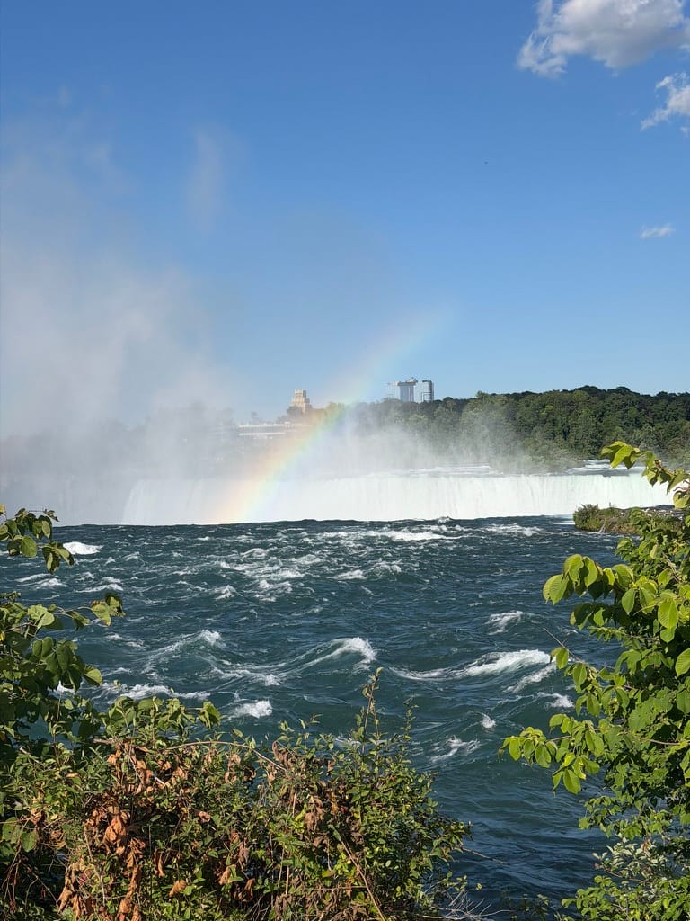 A view from the top of the falls with the water in the foreground and mist and a rainbow in the back.