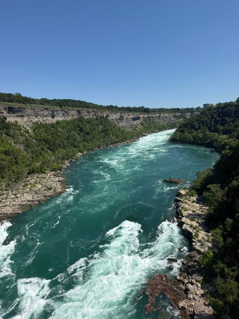 Looking down the gorge toward the falls with the falls out of view. The water is a gorgeous aqua blue and there are trees lining the banks.