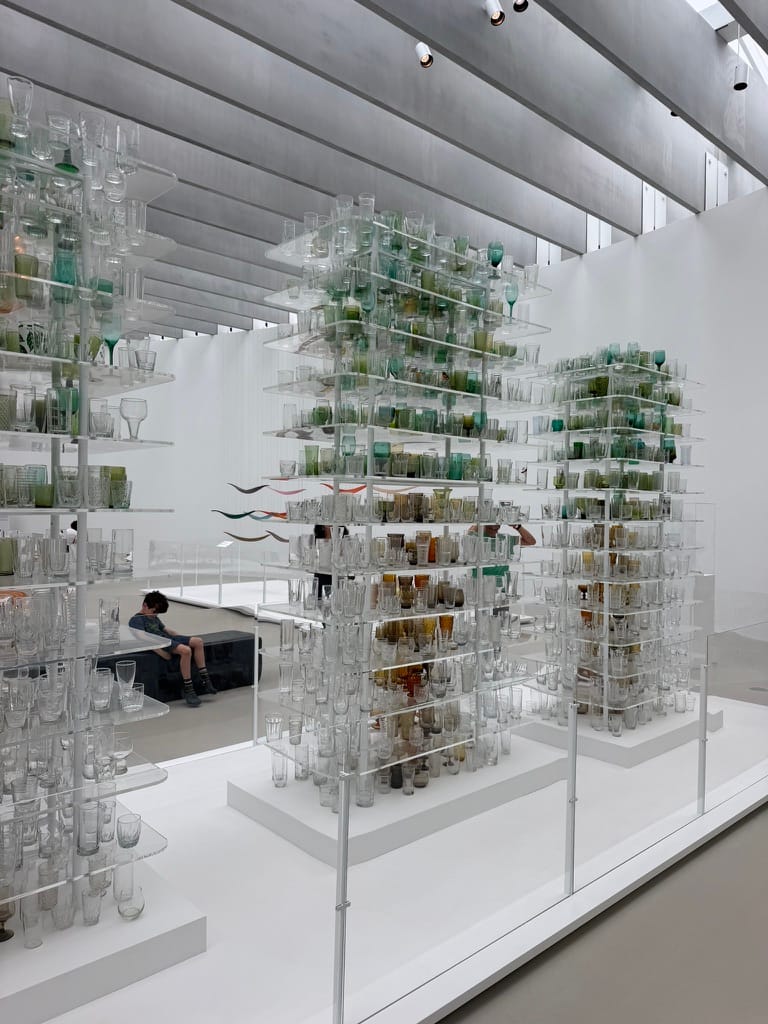 An art piece made of shelves of glass containers. They form the shape of trees using the color.