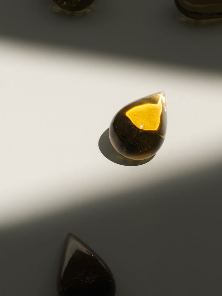 A drop of honey colored glass highlighted in a patch of light. There are other similar pieces of glass in the shadows.